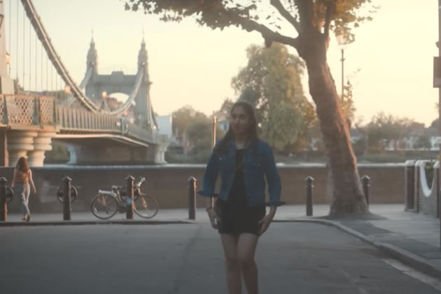 Emma (Ambika Mod) leaving her flat in One Day, with Hammersmith Bridge in the background